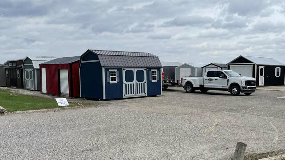 Row of storage sheds on display at an outdoor lot with a delivery truck