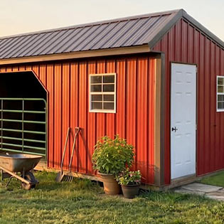 Red metal livestock shelter with gated stall and white side door 