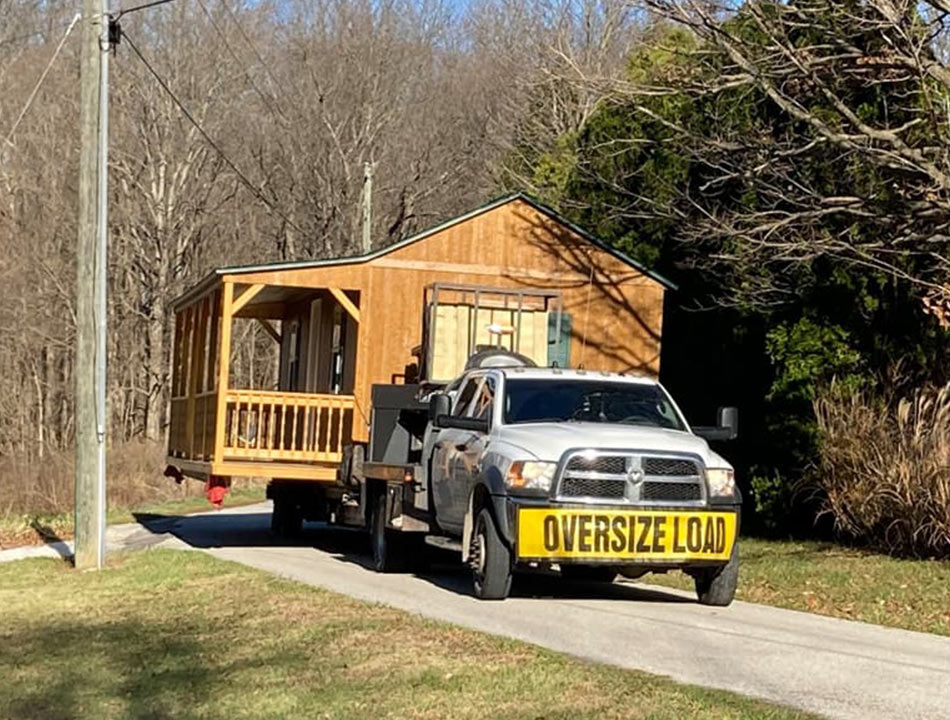 Flatbed truck transporting a wooden cabin with an oversize load sign 